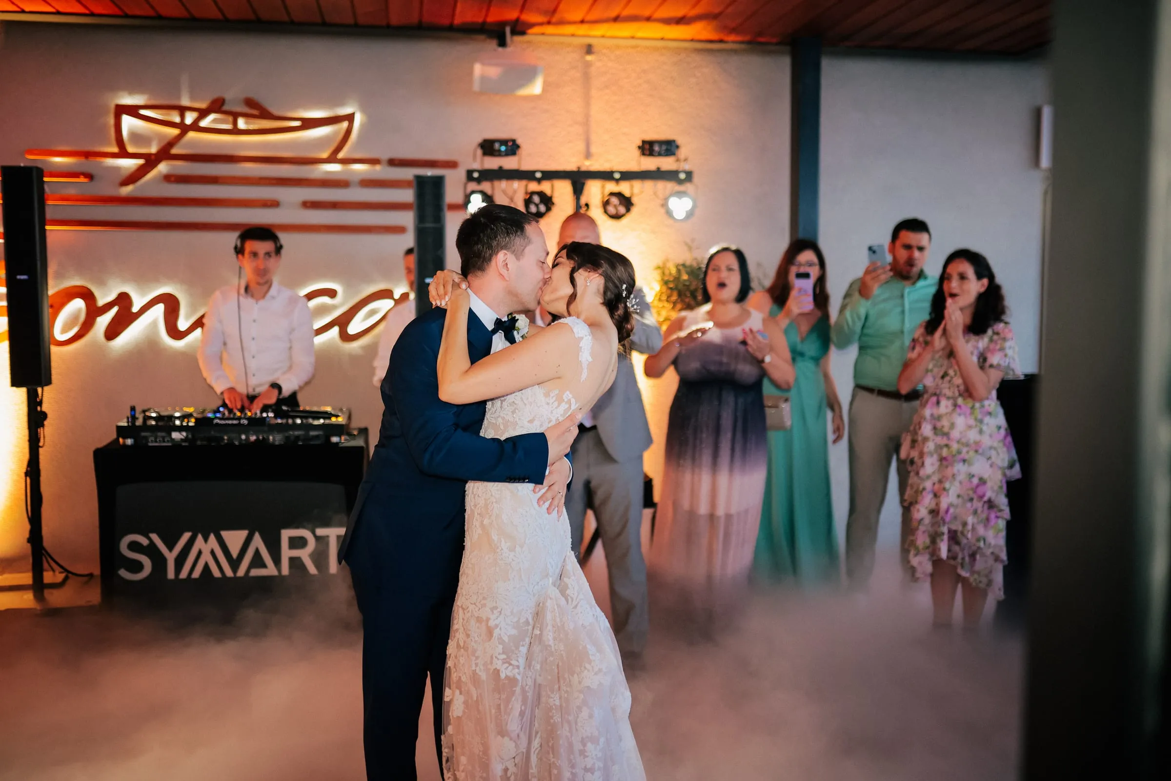 Newlyweds kissing in low fog on the dance floor at Bonaca in Pula while guests film