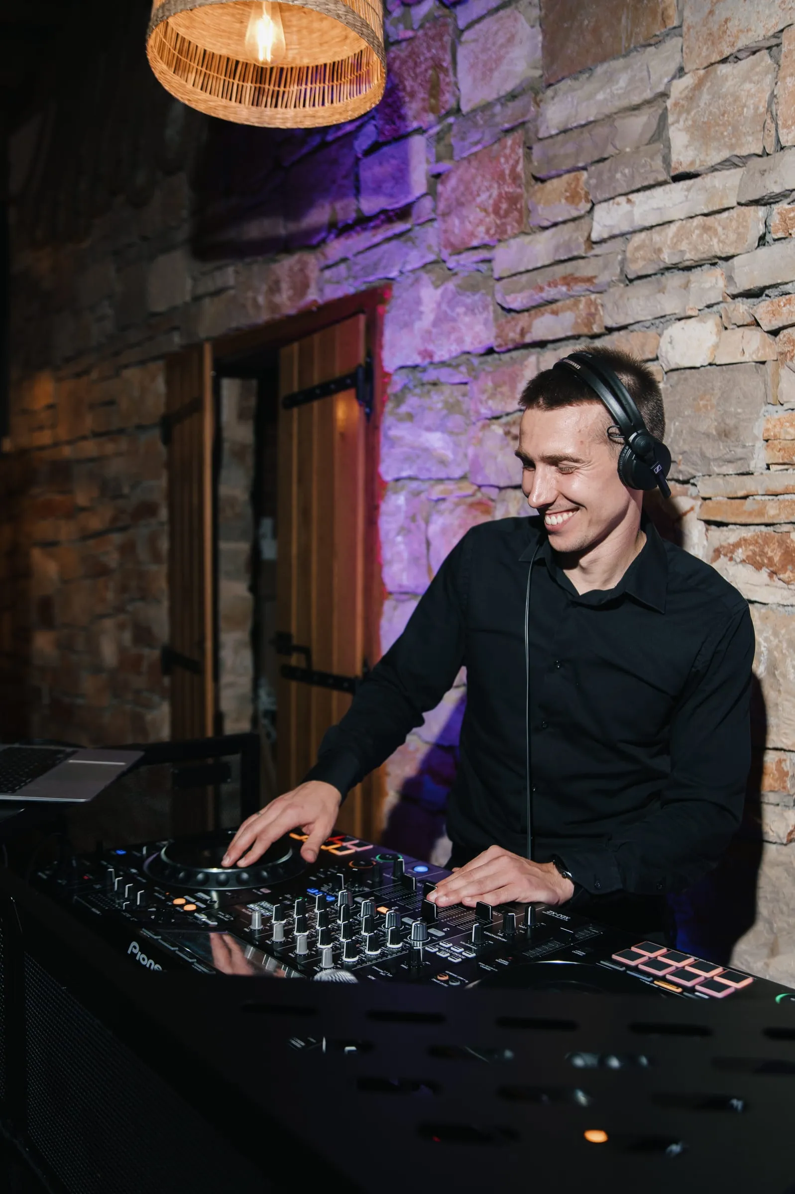 DJ Symart smiling at the decks against a stone wall at Mina in Jelsa
