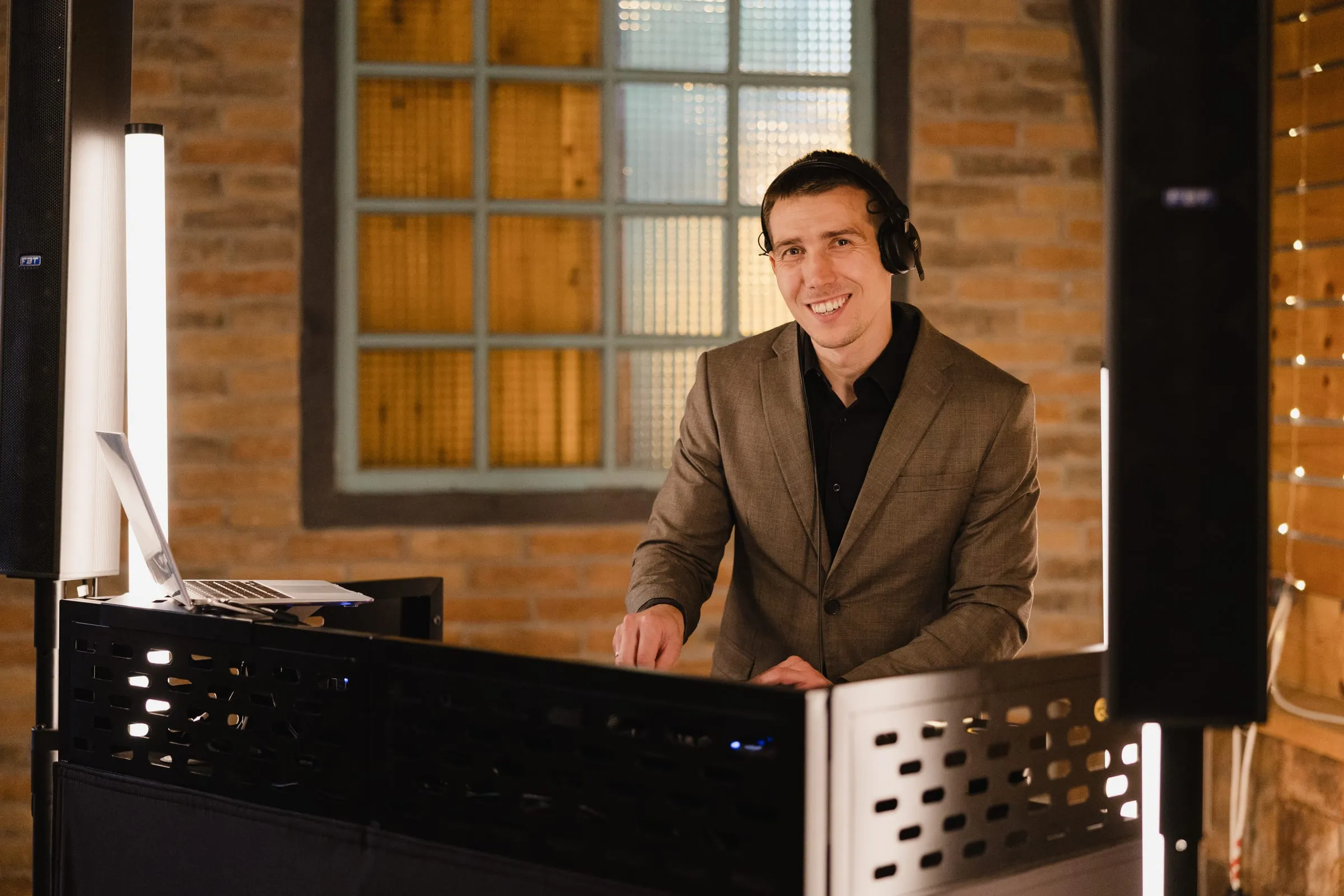 DJ Symart in a tailored jacket smiling behind his DJ booth