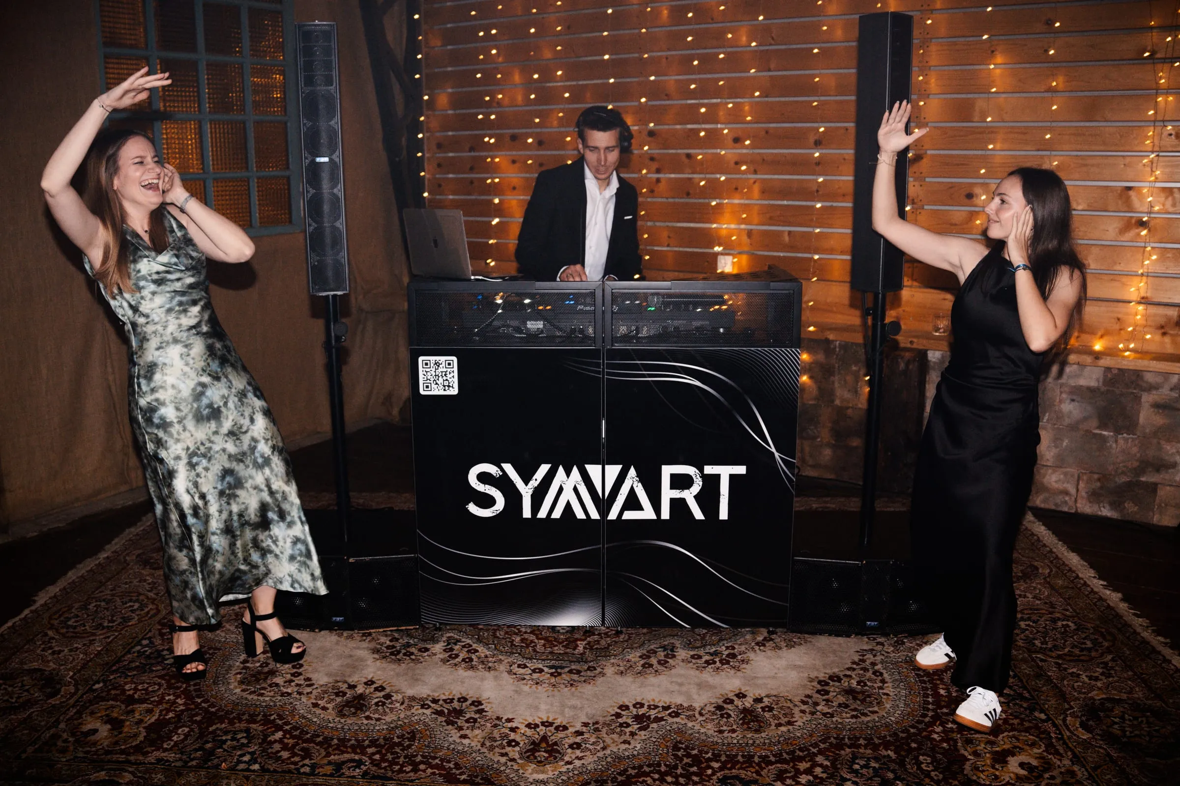Two guests dancing in front of the DJ Symart booth at a wedding