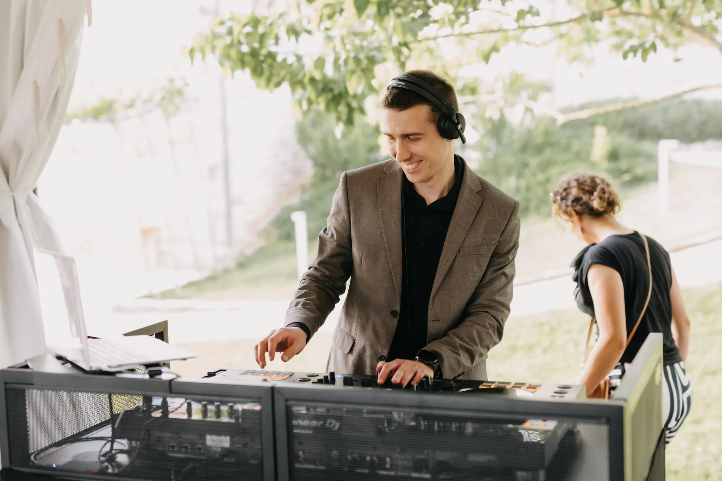 DJ Symart smiling at the decks in the garden of Villa Poropati in daylight